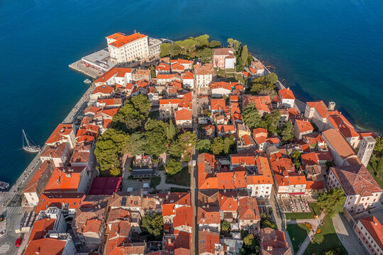 Aerial view of vibrant orange rooftops cascade towards the azure sea, cradling the historic architecture of the old town, Pore&Auml;, Istria County, Croatia.
