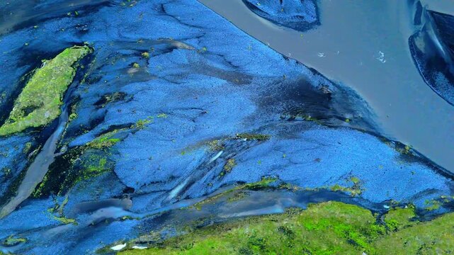 Icelandic streams among vibrant blue grey volcanic roc stones twist like veins on their journey through glaciated valleys and vibrant mossy green flatlands to the sea. Drone aerial birdseye.