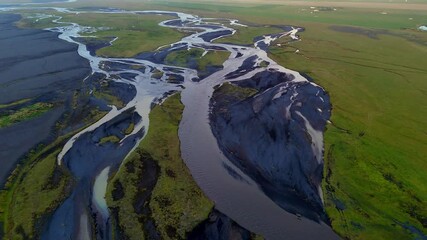 Icelandic streams twist like veins on their journet through glaciated valleys, volcanic rock and vibrant mossy green flatlands to the sea. Drone aerial reveal horizon.