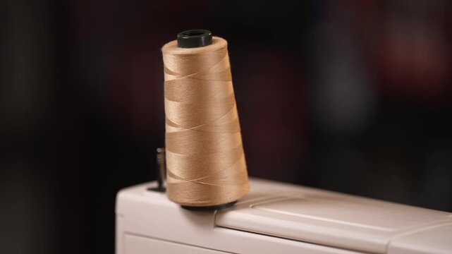 A spool of beige thread sits on a sewing machine, ready for stitching. A minimal, focused look at textile craftsmanship and handmade production.