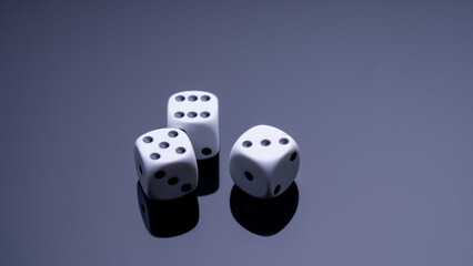 Three white dice are on a dark surface. The dice are arranged in a row, with the middle one slightly larger than the other two. Concept of anticipation and excitement