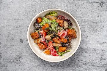 Fresh chicken salad with crispy fried pieces, lettuce, tomatoes, mixed greens, and dressing served in a ceramic bowl on gray background