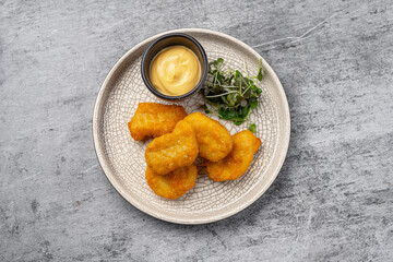 Golden crispy chicken nuggets served with creamy dipping sauce and fresh microgreens on a white ceramic plate with cracked texture on gray background