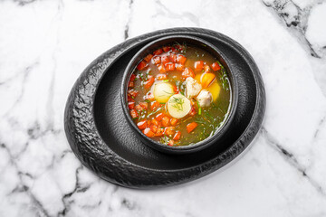 Traditional fish soup with potatoes, carrots, red pepper, and herbs served in a black ceramic bowl on marble table