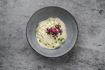 Creamy gourmet mousse with microgreens and herb oil drops served in gray ceramic bowl on stone background