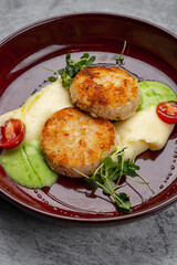 Two golden brown chicken cutlets served with mashed potatoes, green pea puree, cherry tomatoes and microgreens on a red ceramic plate