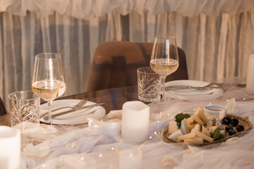 Romantic Dinner Setting with Wine Glasses, Cheese Plate, and Candles: Warm Indoor Mood, Soft Lighting, Elegant Table Decor, Beige and Gold Tones.