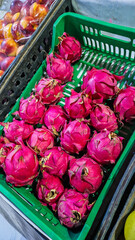 A basket filled with vibrant pink dragon fruits at a market. The fruits have a unique shape and green spiky leaves, showcasing their exotic appearance.