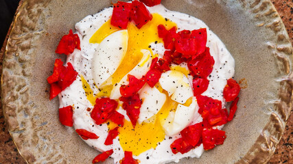 A plate of scrambled eggs topped with sliced cherry tomatoes. The dish is garnished with black pepper and served on a textured ceramic plate.