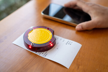 Restaurant queue pager placed on receipt on wooden table. Perfect for concepts of food service technology, customer waiting system, smart restaurant operations, and digital order notification tools.