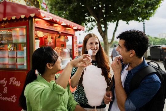 Friends eating cotton candy at a cheerful summer food stall outdoors