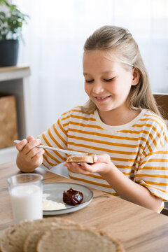 Child spreading jam on bread at breakfast in a bright kitchen