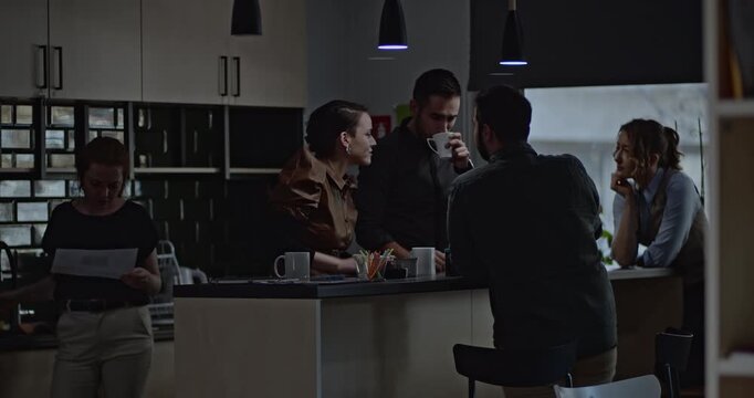 Students and young professionals chat and drink coffee in an office break room. They're discussing something related to their work or studies.