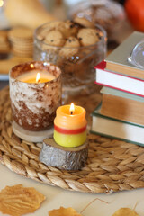 Lit candles, cookies, chocolate, nuts, tea, wine, pumpkins, books, reading glasses and autumn leaves on the table. Autumnal hygge at home. Selective focus.