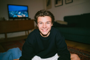 Young man in casual hoodie playing video games at home on bed with relaxed expression
