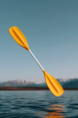 Bright orange kayak paddle floating in mid-air above calm lake with mountain background at sunrise
