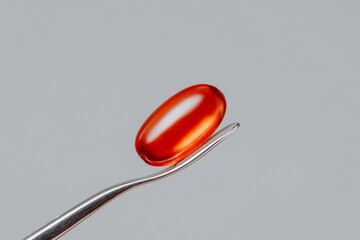 Translucent amber capsule held by tweezers on neutral background, macro pharmaceutical supplement and clinical research detail