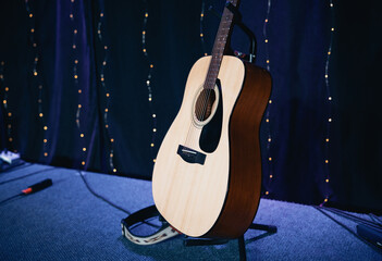 Beautiful acoustic guitar resting on a stand on a darkened stage floor, illuminated by a warm spotlight. Perfect for folk, country, live music, and intimate performance concepts.