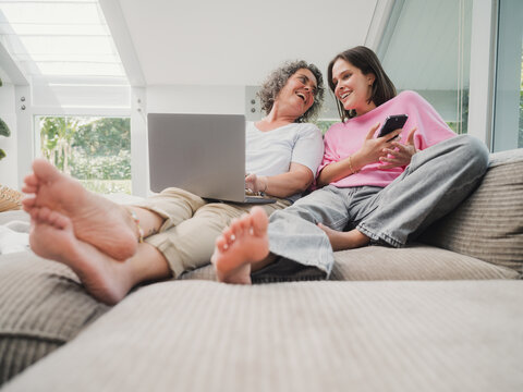 Mother and daughter cuddling on couch with laptop and smart phone at home