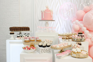 Stylish dessert table with pink cake, cupcakes, and balloons. Perfect for baby shower, birthday, or wedding. Elegant white and pink pastel tones create luxury festive atmosphere. High quality photo