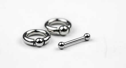 A collection of professional silver body piercing jewelry, including two captive bead rings and a straight barbell, isolated on a clean white background