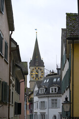 Citycape with alley and church tower with clock face of Saint Peter church at the old town of Swiss city of Zürich on cloudy and rainy autumn day. Photo taken October 27th, 2025, Zurich, Switzerland.
