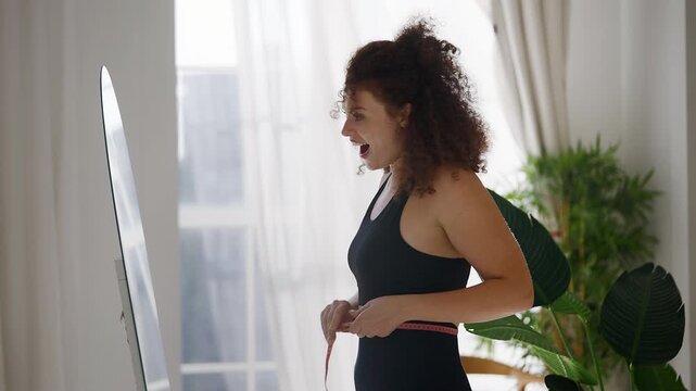 Athletic woman measuring waist in mirror, feeling confident about her body