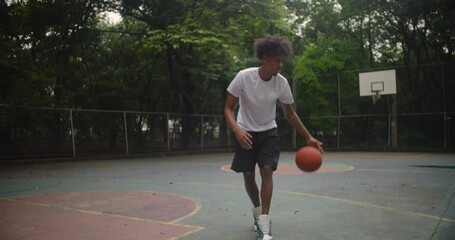 African descent man dribbling basketball on outdoor urban court, showing focus, rhythm, and relaxed energy during solo practice in city park setting - Powered by Adobe
