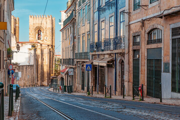 Empty tram street in Alfama district with traditional azulejos tiled buildings and Lisbon Cathedral in Lisbon city, Portugal. Medieval alley in old town of Lisboa. Travel and tourism in Europe