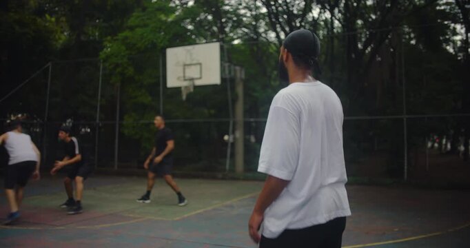 African descent man wearing durag turns to join group of friends playing basketball on outdoor city court, expressing camaraderie, energy, and urban athletic lifestyle