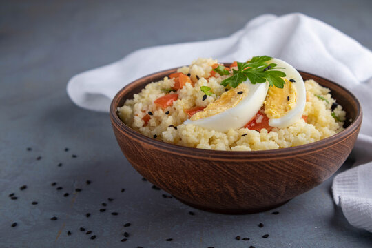 Couscous with vegetables and a piece of egg in a clay bowl on a gray background. Space for text.