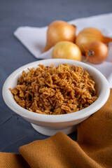sliced fried onions in a bowl on a brown towel and gray background