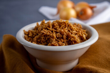 sliced fried onions in a bowl on a brown towel and gray background