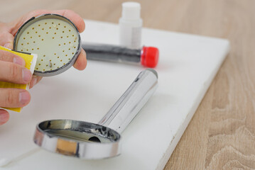 Closeup photo of male hands fixing modern rain shower head. Cleaning shower head filter using sandpaper, simple home fix tutorial