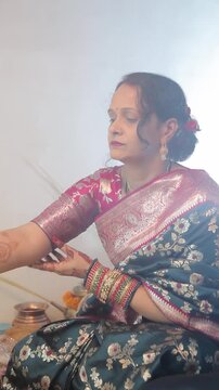 An Indian woman in a blue saree offering puja with a traditional thali during a festival