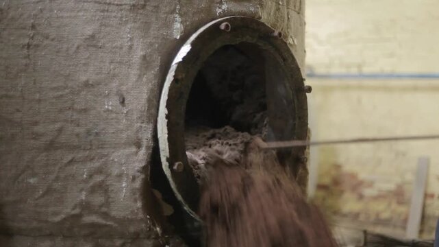 Worker cleaning biomass (plant residue) from industrial distillation chamber after essential oil extraction