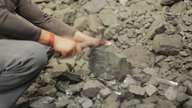 Worker crushing hard coal pieces with a hammer in an industrial environment
