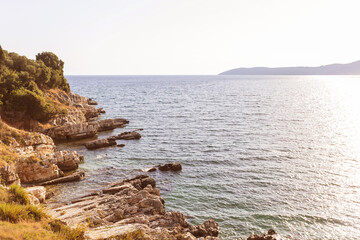 Golden hour over rocky cliffs and calm sea with distant hills and trees