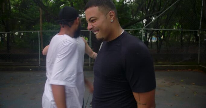 Friends greeting each other with dap handshake on outdoor basketball court, expressing friendship, respect, and camaraderie in casual urban sports setting