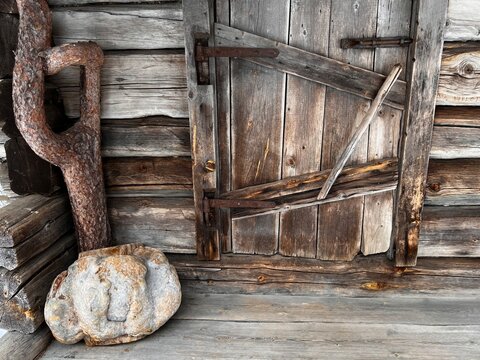 Background: door of a small, rustic wooden cabin with wood paneling, a wooden floor, a wooden sculpture, and a large stone in the corner to the left of the entrance.