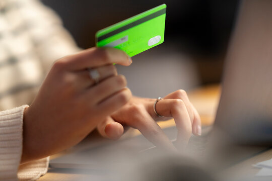 Crop anonymous young woman using green plastic card for online shopping on internet website at home