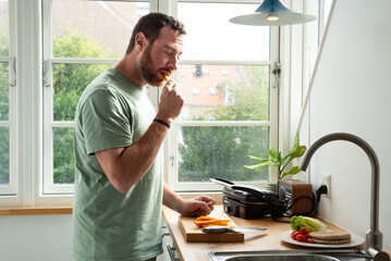 Man eating cheese while is preparing his lunch in a scandinavian style  kitchen.