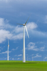 Fototapeta premium Group of wind turbines in green field under blue sky