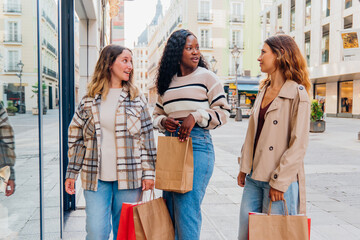 Diverse group of young women friends happily walking along an urban shopping street, carrying paper bags, enjoying leisure time and a conversation after a day out