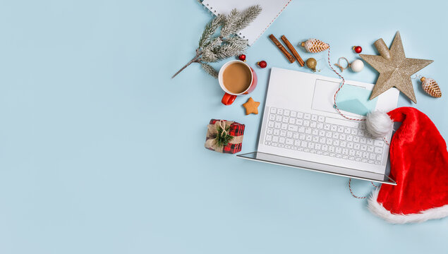 Top view of a laptop on a table with an isolated blue background for mockup flat lay in Christmas time. Christmas tree, gifts, decorations in background. New year concept in office.