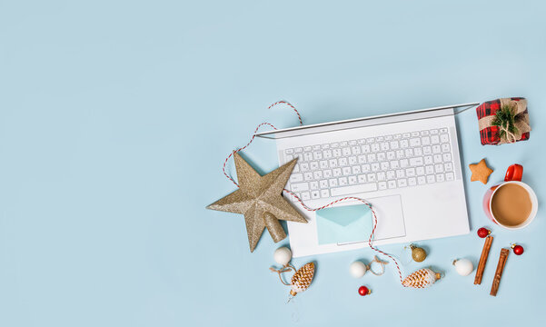 Top view of a laptop on a table with an isolated blue background for mockup flat lay in Christmas time. Christmas tree, gifts, decorations in background. New year concept in office.
