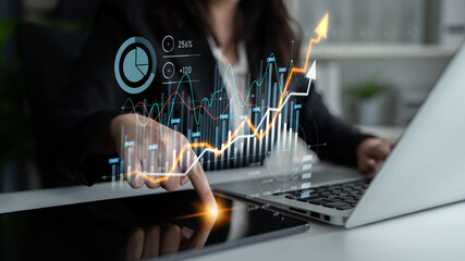 A businesswoman is analyzing financial data with digital graphs on her laptop and interacting with...