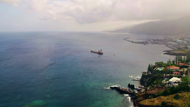 Large ship anchored ocean shore by cozy coastal town cloudy day aerial view. - Powered by Adobe