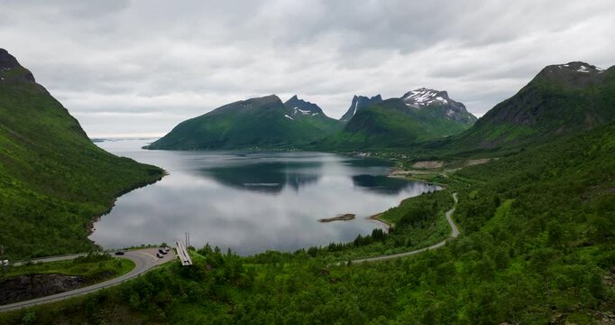 Aerial view Bergsbotn viewpoint in Senja, Norway, showing majestic fjords, snow-capped peaks, lush green forests, and winding coastal roads under overcast skies