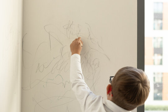 A child scribbles with a pencil on a white wall in a house, children's art